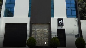 Um edifício moderno com uma entrada ampla, duas portas pretas e uma placa indicando 'DUE 179'.