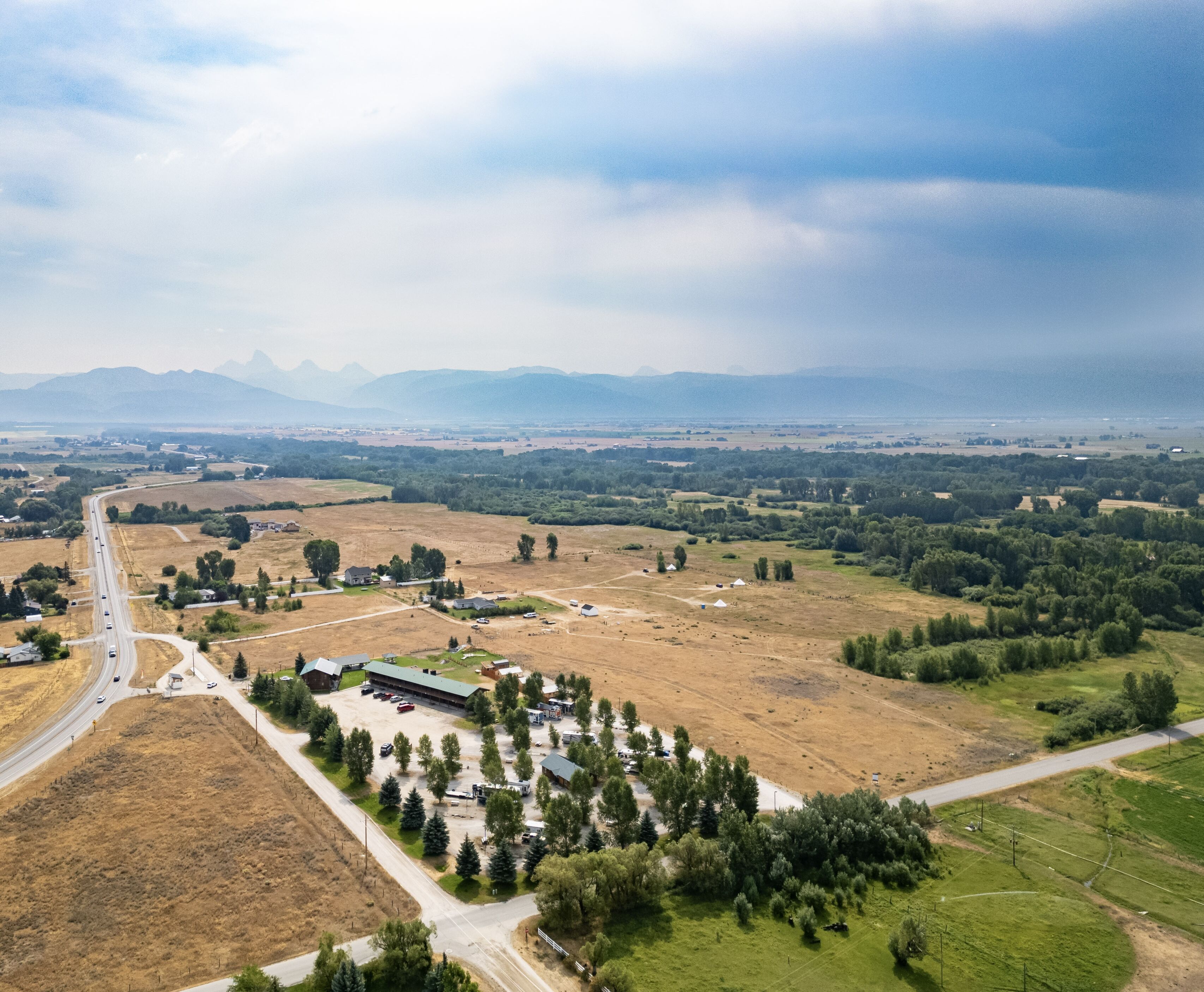 Vista aérea de uma zona rural com uma estrada principal, campos e edifícios dispersos.