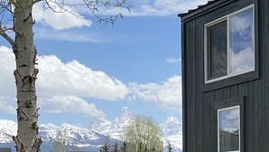 En moderne bygning med stort vindue, træhegn og et baggrund af snedækkede bjerge.