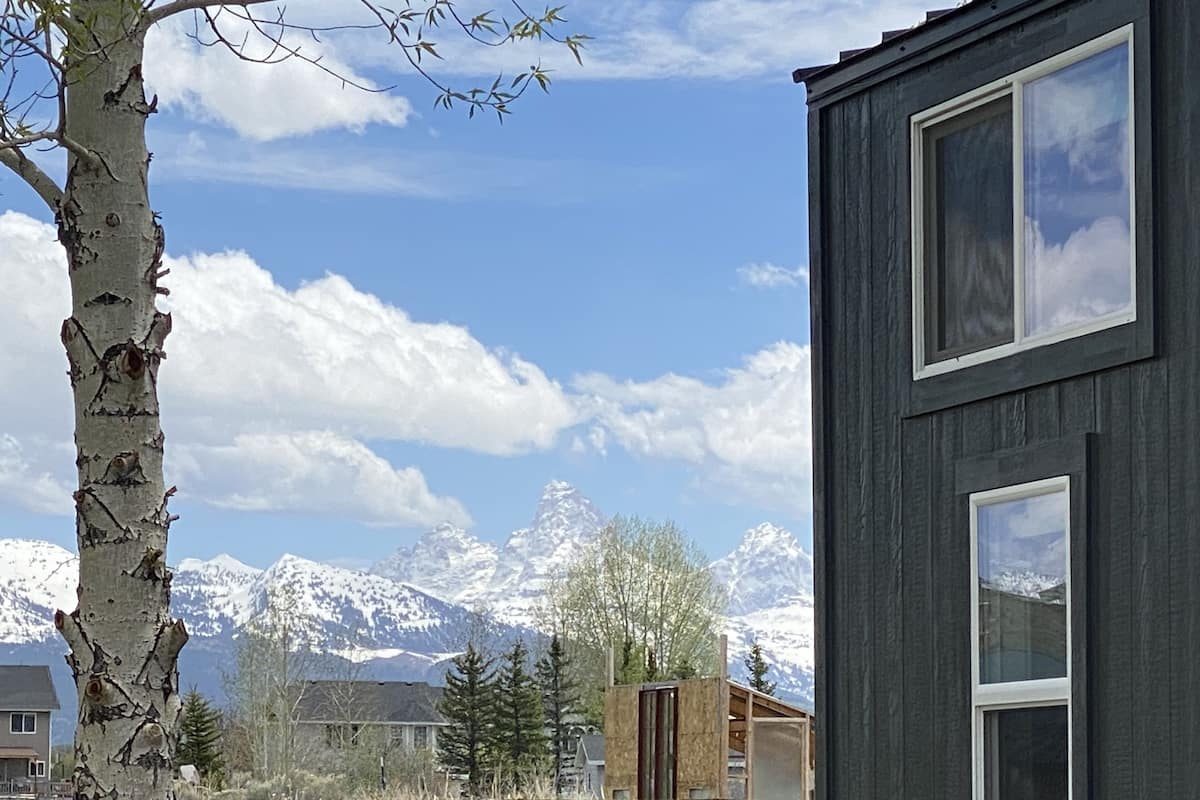 A modern building with a large window, a wooden fence, and a backdrop of snow-capped mountains.