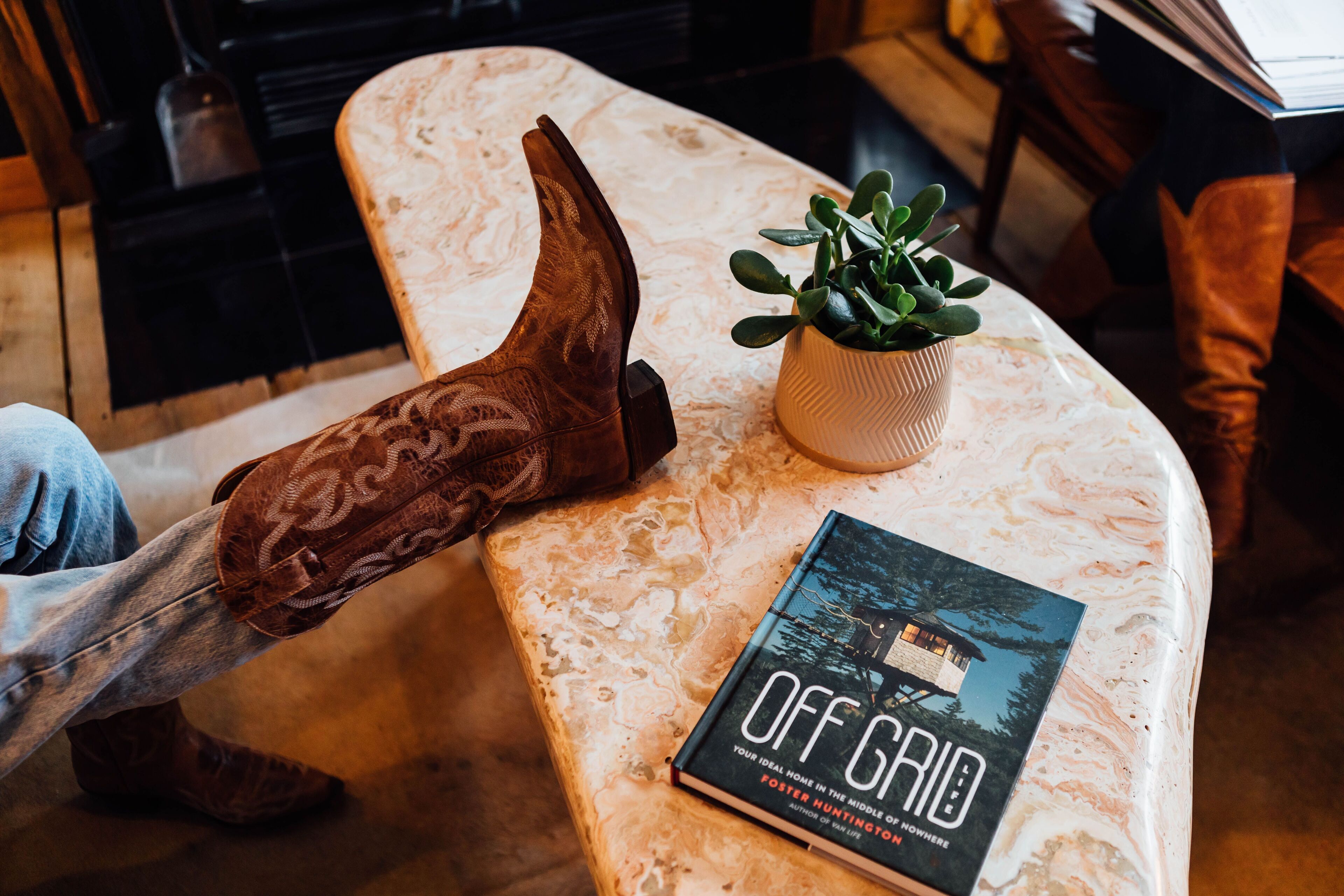 A book titled 'Off Grid' on a marble table with a rustic wooden shoe and a small potted plant.