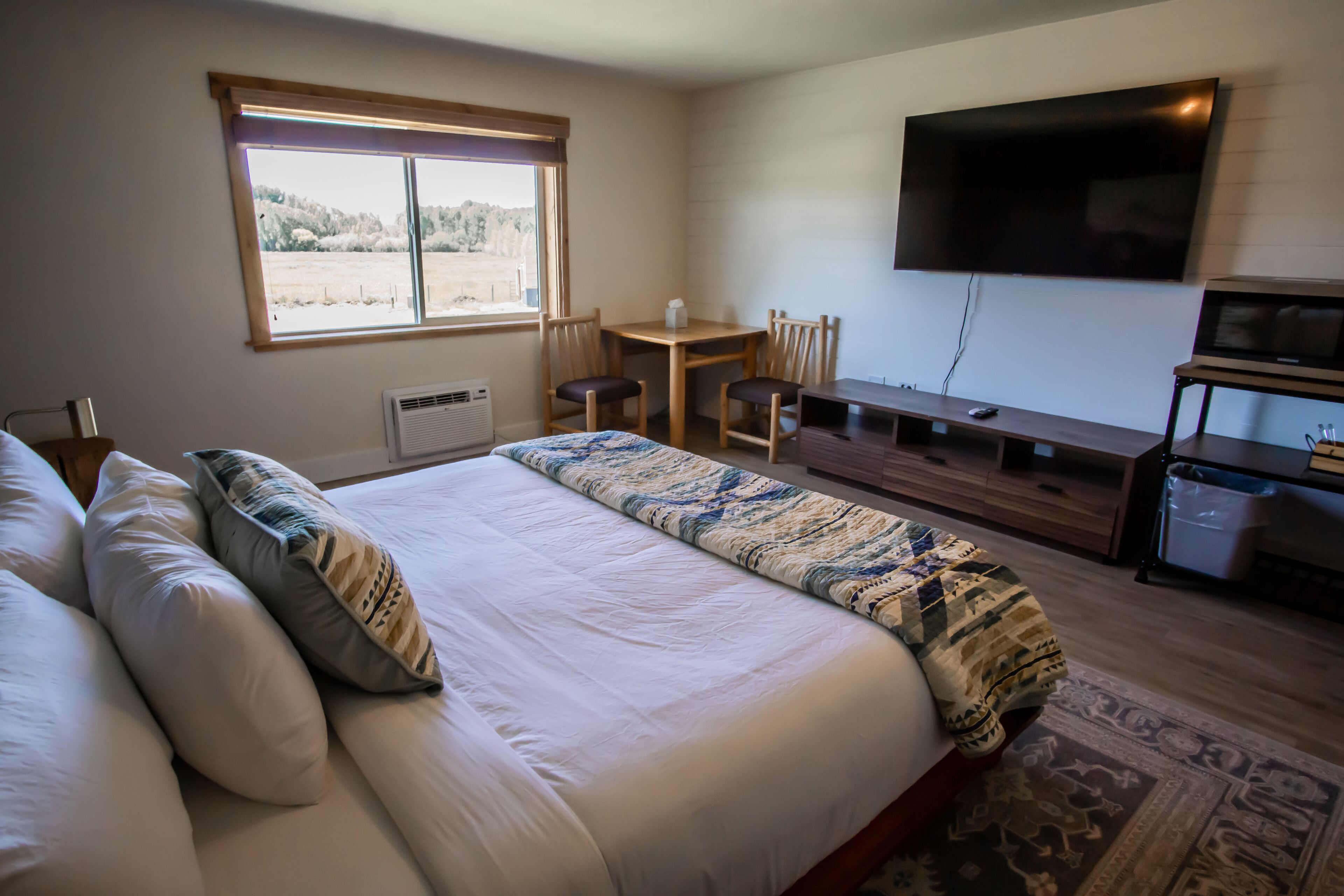 A bedroom with a large bed, a desk, a TV, and a window with a view of trees.