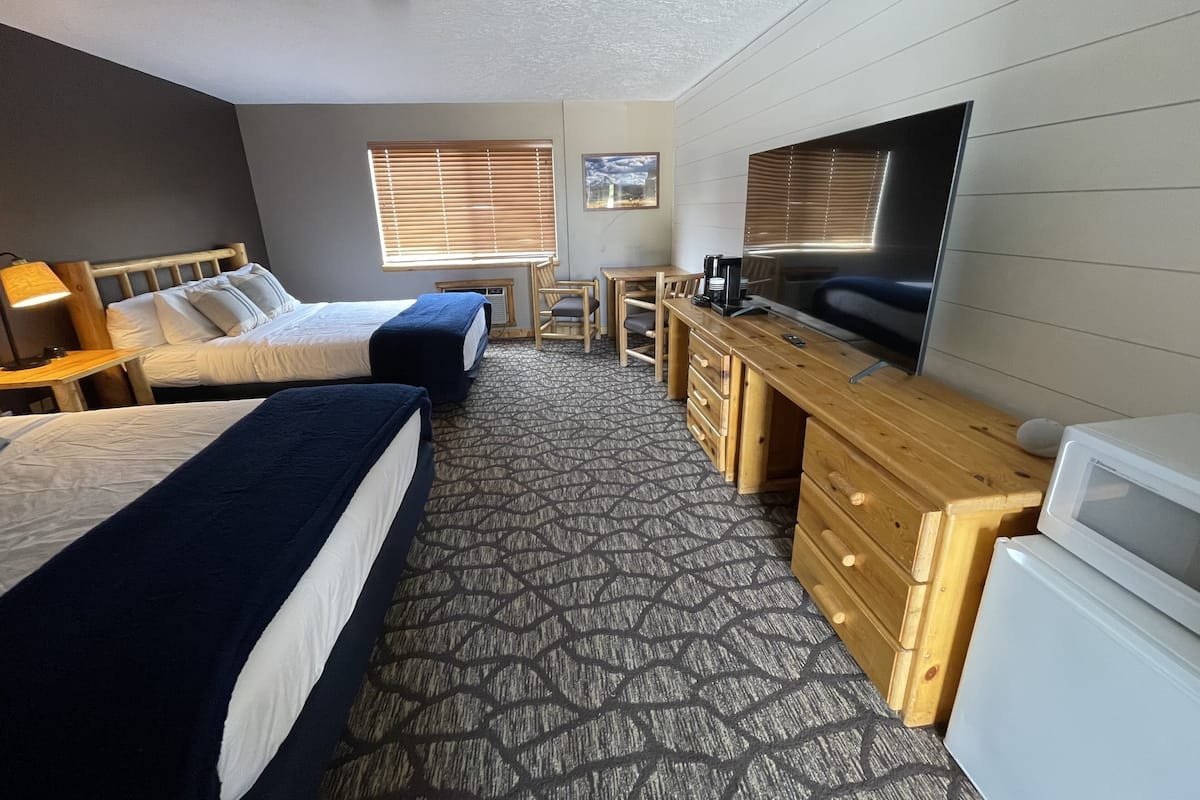 A hotel room with two beds, a desk, a television, and a microwave.