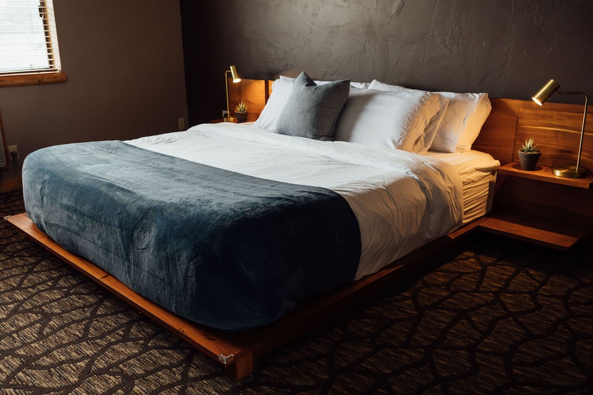 A bed with a wooden frame, a patterned carpet, and two bedside lamps.