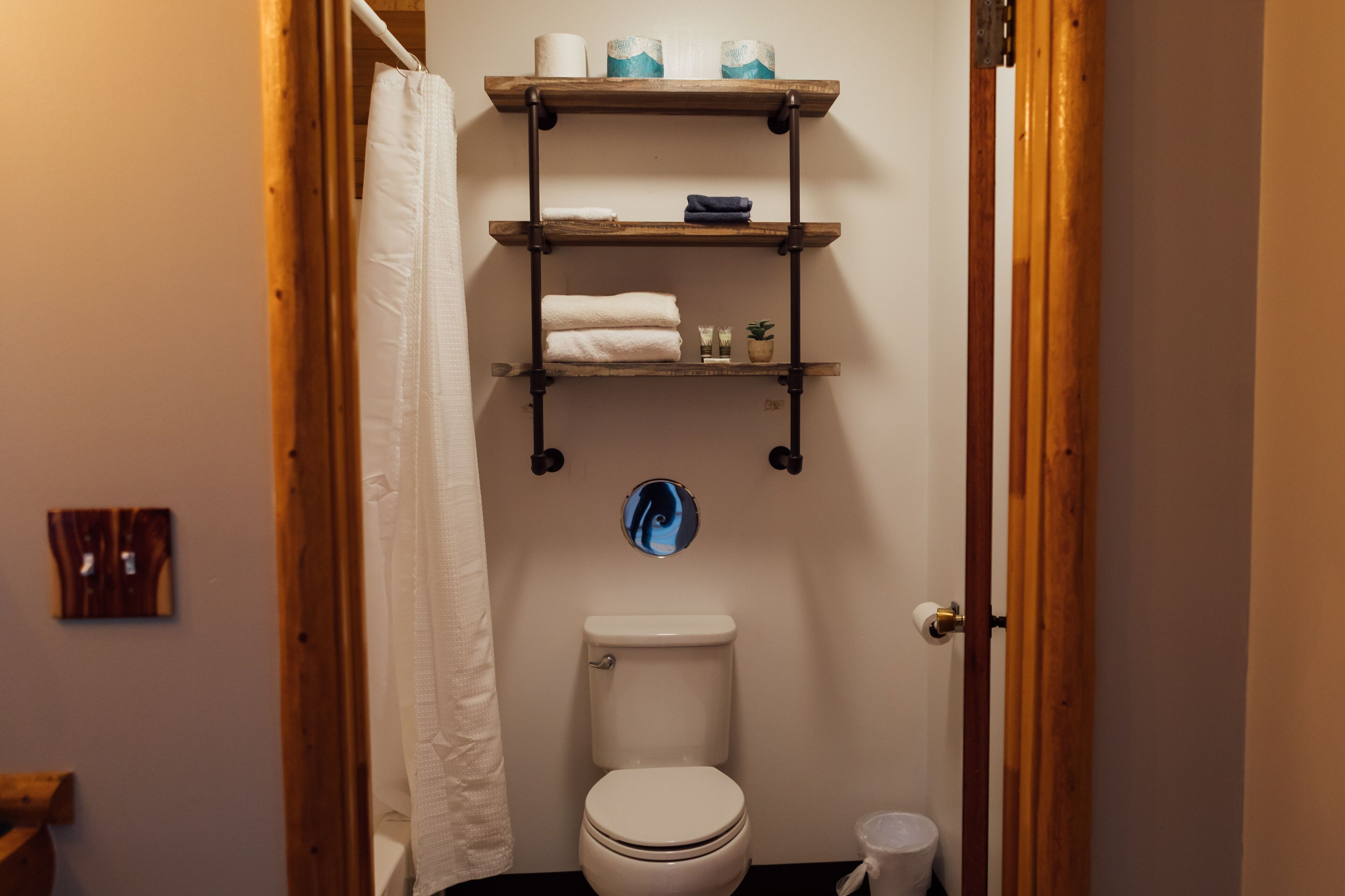 Un baño con inodoro, un estante con toallas y una pequeña planta.