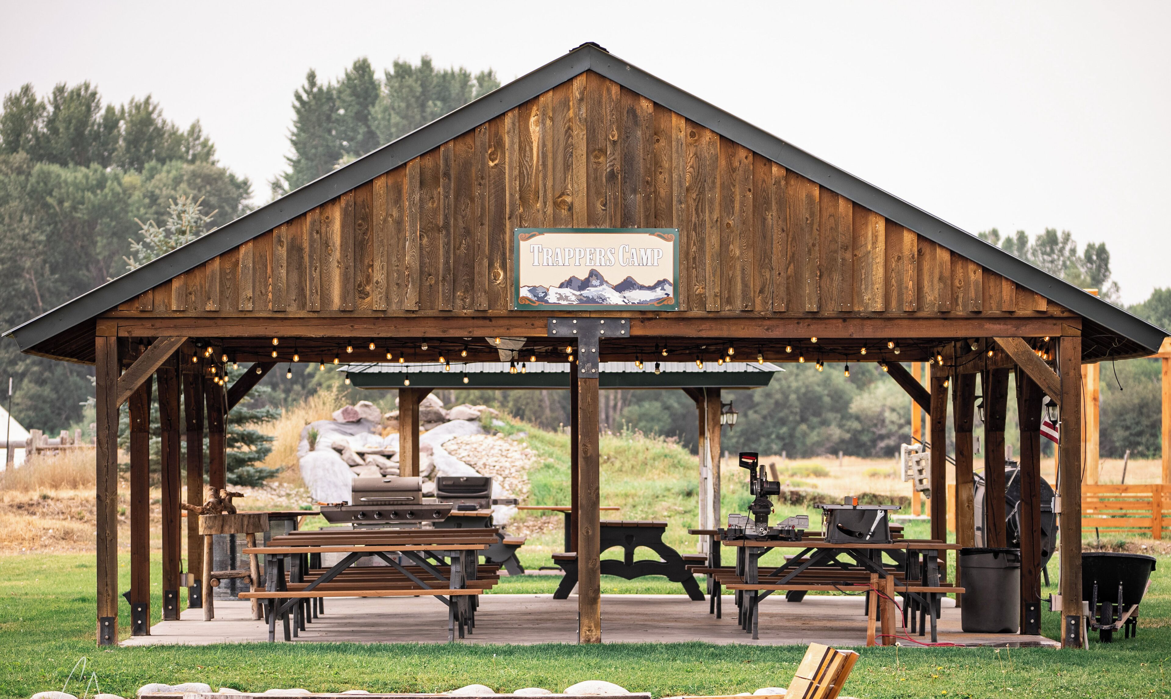 A rustic wooden structure labeled "Trappers Camp" with picnic tables and barbecue equipment.