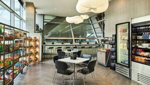 A modern cafe with a central table and chairs, surrounded by shelves stocked with snacks and beverages.