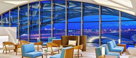 A modern lounge area with seating and a large window offering a view of a cityscape.