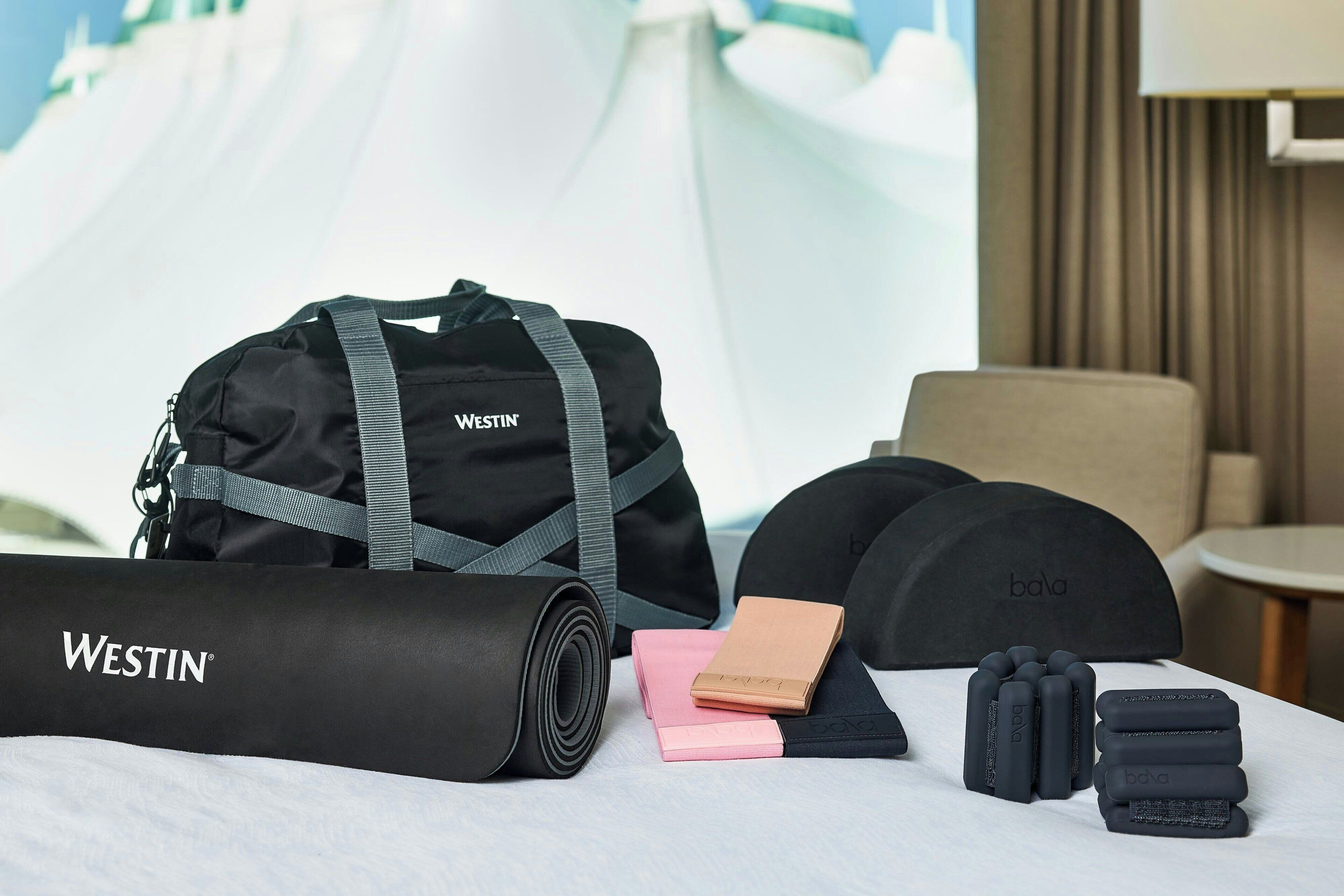 A neatly arranged room with a yoga mat, a Westin branded bag, a pink notebook, and a set of black headbands.