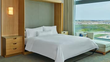 A hotel room with a large bed, wooden nightstands, a seating area with a view of an airport.