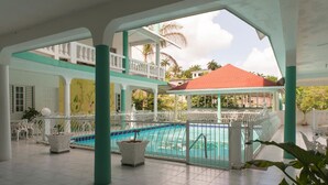 A covered swimming pool area with a view of a red-roofed building, white railings, and potted plants. - Diamond Villas and Suites (Montego Bay)