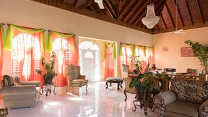 A spacious living room with a high ceiling, large windows with curtains, and several pieces of furniture including sofas and chairs. - Diamond Villas and Suites (Montego Bay)