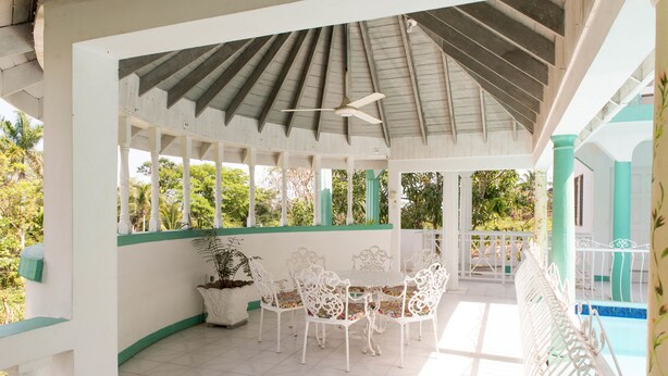 A covered patio with white metal chairs and a table, surrounded by white walls and a green railing. - Diamond Villas and Suites (Montego Bay)