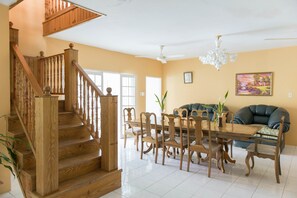 Amplia sala de estar con una escalera de madera, una mesa de comedor con sillas, un sofá y una lámpara de araña.