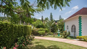 A well-maintained garden with a pathway leading to a building with a red roof and green accents. - Diamond Villas and Suites (Montego Bay)