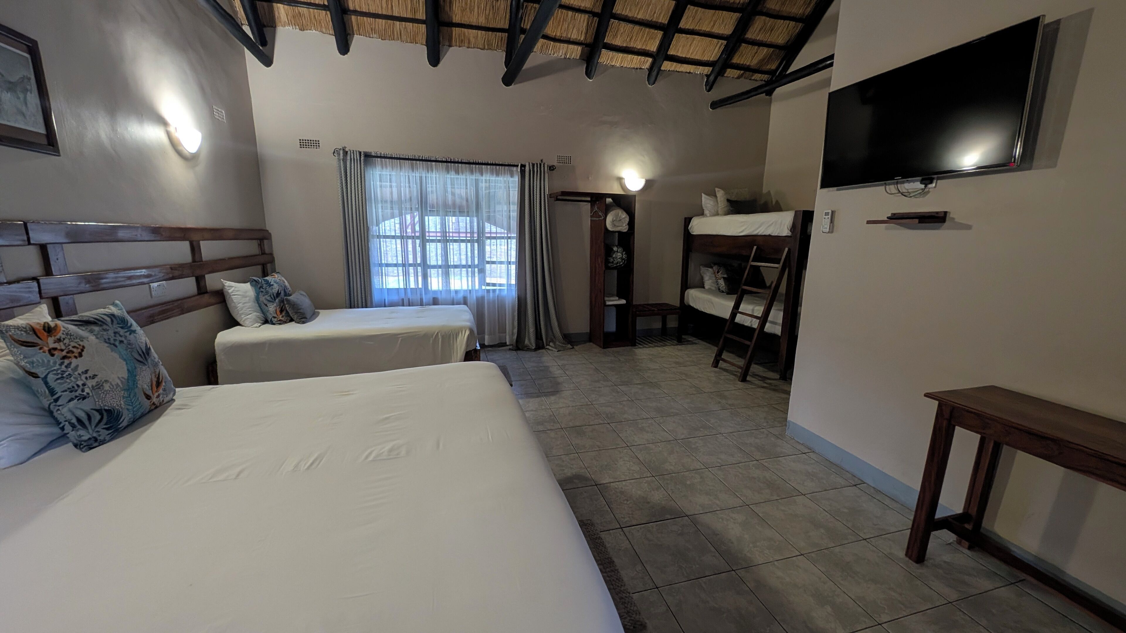 A hotel room with two beds, a TV, a window with curtains, and a tiled floor.