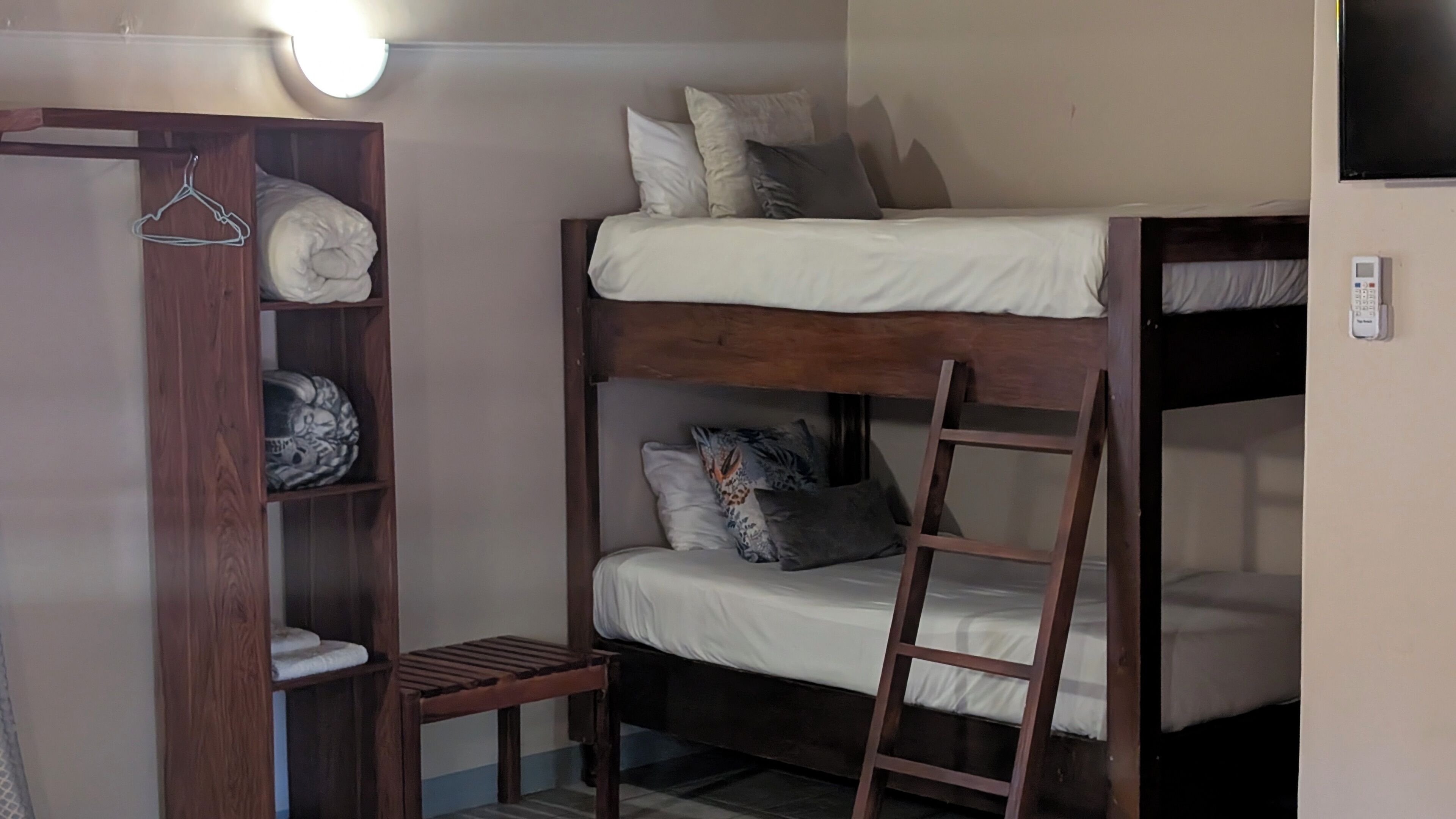 A bunk bed room with a wooden wardrobe, a ladder, and a hanging clothes rack.