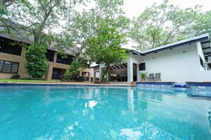 Ein Swimmingpool mit klarem, blauem Wasser, umgeben von einem Gebäude mit einer gefliesten Terrasse und einem Baum.