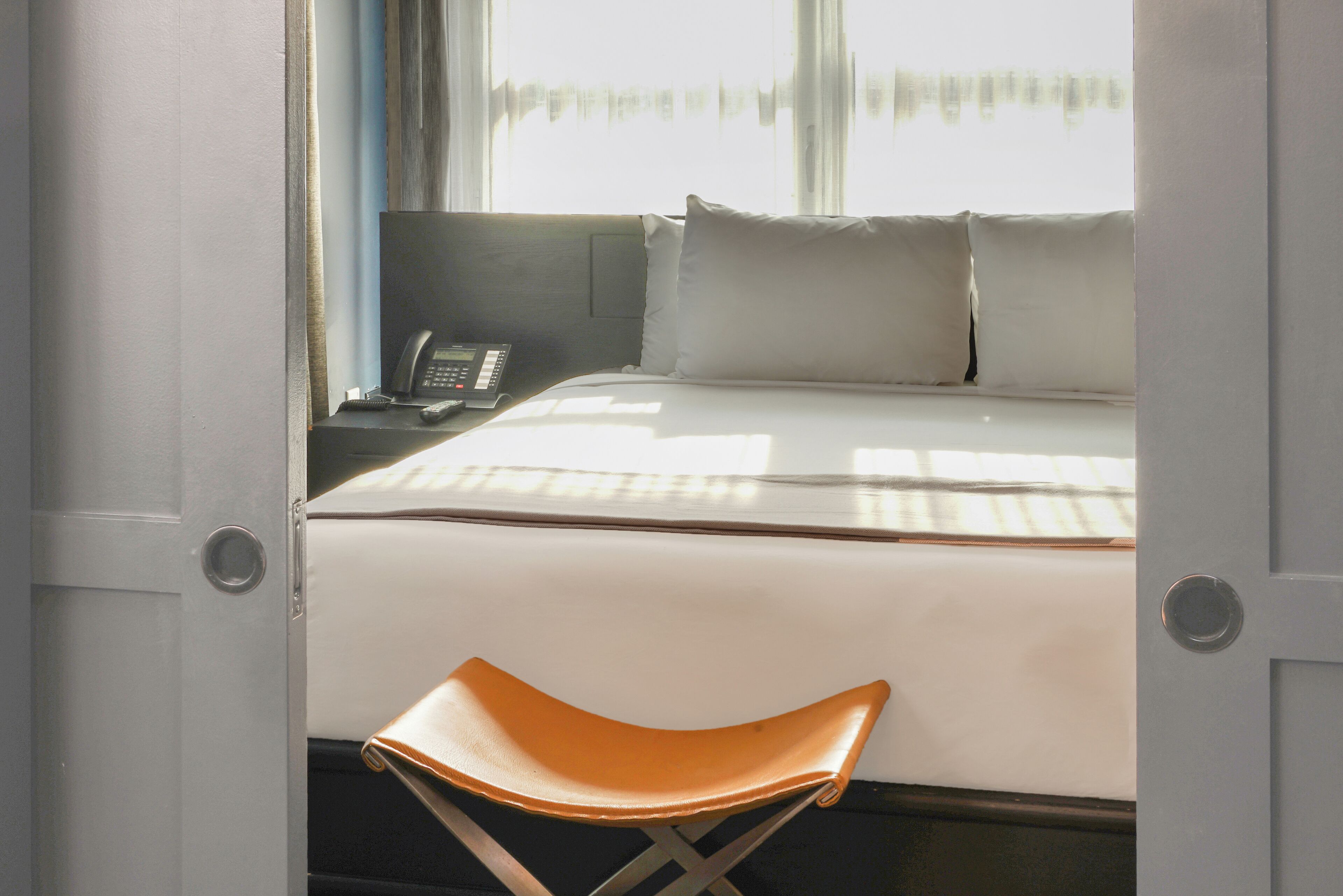 A hotel room with a bed, a bedside table with a phone, and a window with curtains.