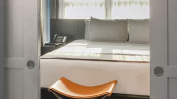 A hotel room with a bed, a bedside table with a phone, and a window with curtains.