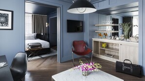 A modern hotel room with a bed, a desk, a chair, a dining table, and a kitchen area.