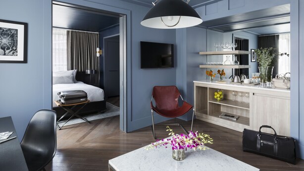 A modern hotel room with a bed, a desk, a chair, a dining table, and a kitchen area. - The Tillary Hotel (Brooklyn)