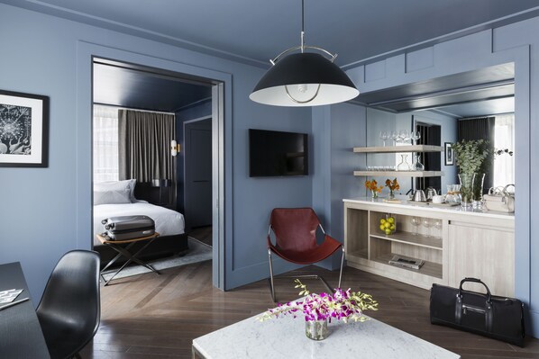 A modern hotel room with a bed, a desk, a chair, a dining table, and a kitchen area. - The Tillary Hotel (Brooklyn)