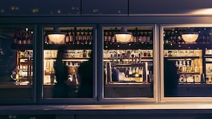 A bar with shelves of bottles and glasses, illuminated by hanging lamps.