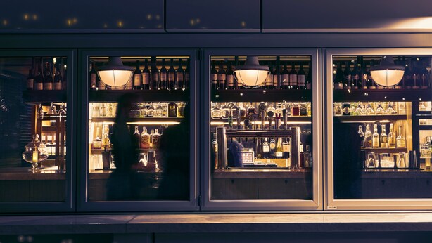 A bar with shelves of bottles and glasses, illuminated by hanging lamps. - The Tillary Hotel (Brooklyn)