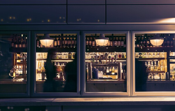 A bar with shelves of bottles and glasses, illuminated by hanging lamps. - The Tillary Hotel (Brooklyn)