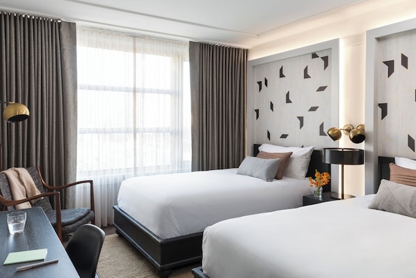 A hotel room with two beds, a desk, a chair, a lamp, and a window with curtains.