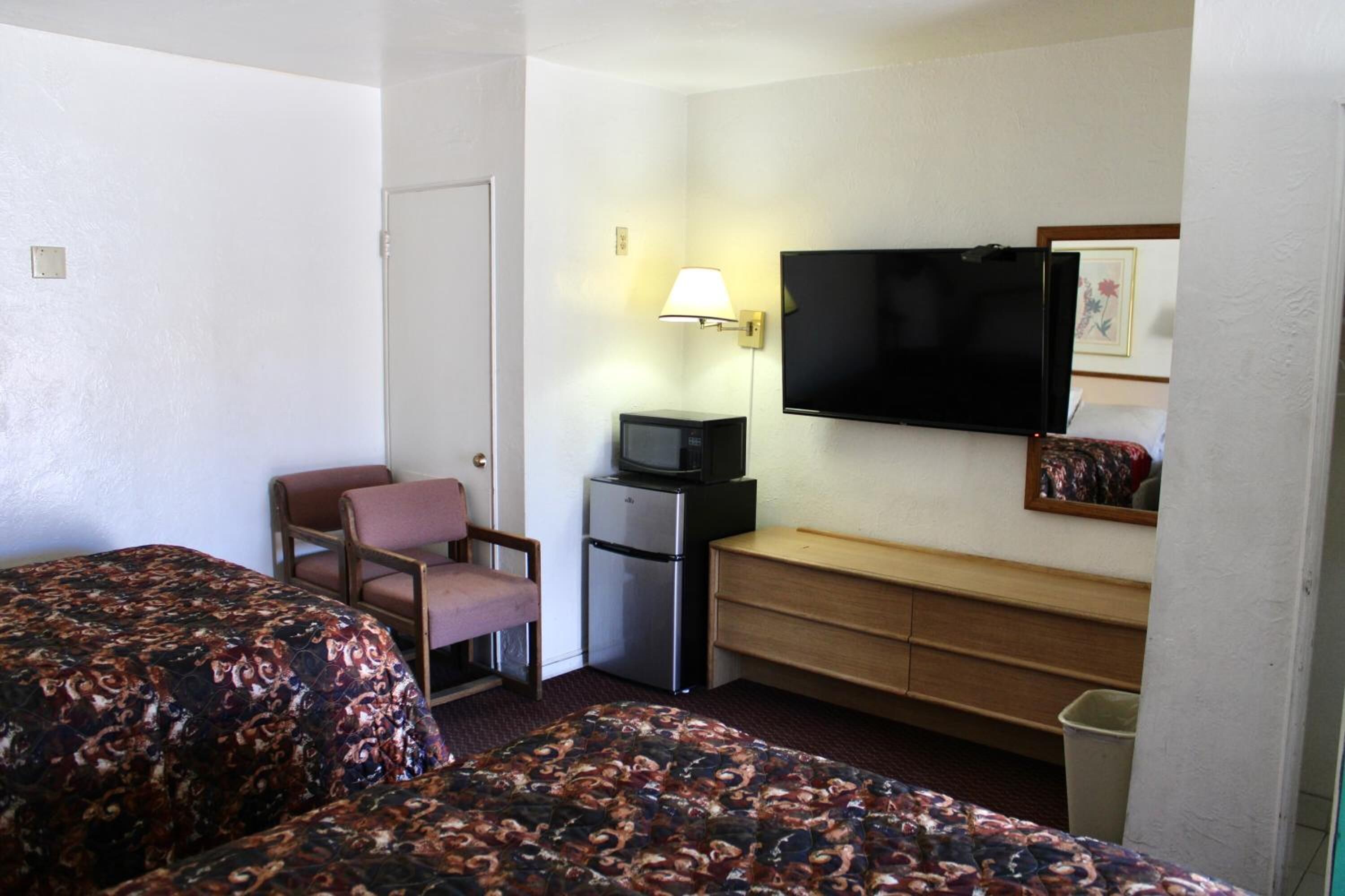 A hotel room with two beds, a television, a desk, a chair, and a small refrigerator.