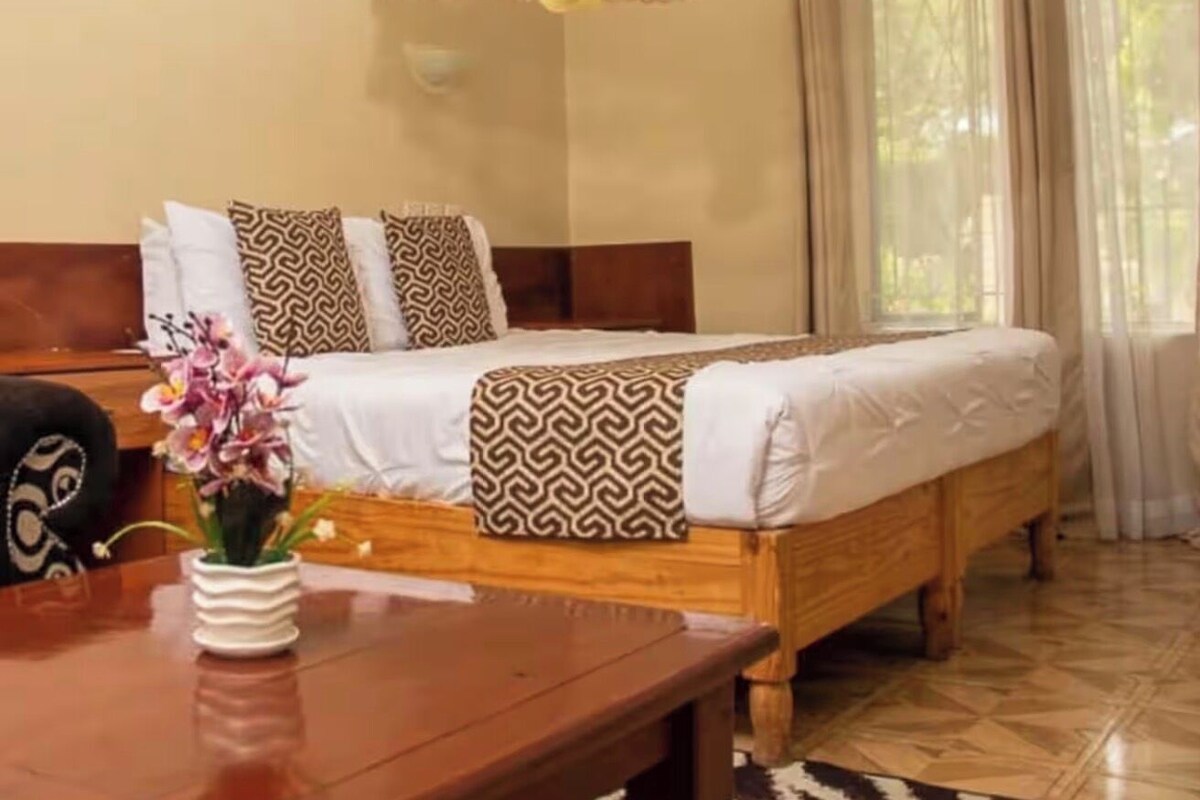 A bed with patterned bedding, a wooden headboard, and a table with a vase of flowers.