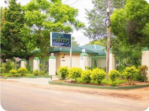 A building with a signboard, surrounded by greenery and a fence.