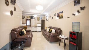 A modern living room with two leather sofas, a small table, and a water dispenser. - Wild Trekkers Lodge (Victoria Falls)