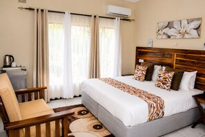 A hotel room with a bed, a chair, a coffee maker, and a large window with curtains. - Wild Trekkers Lodge (Victoria Falls)