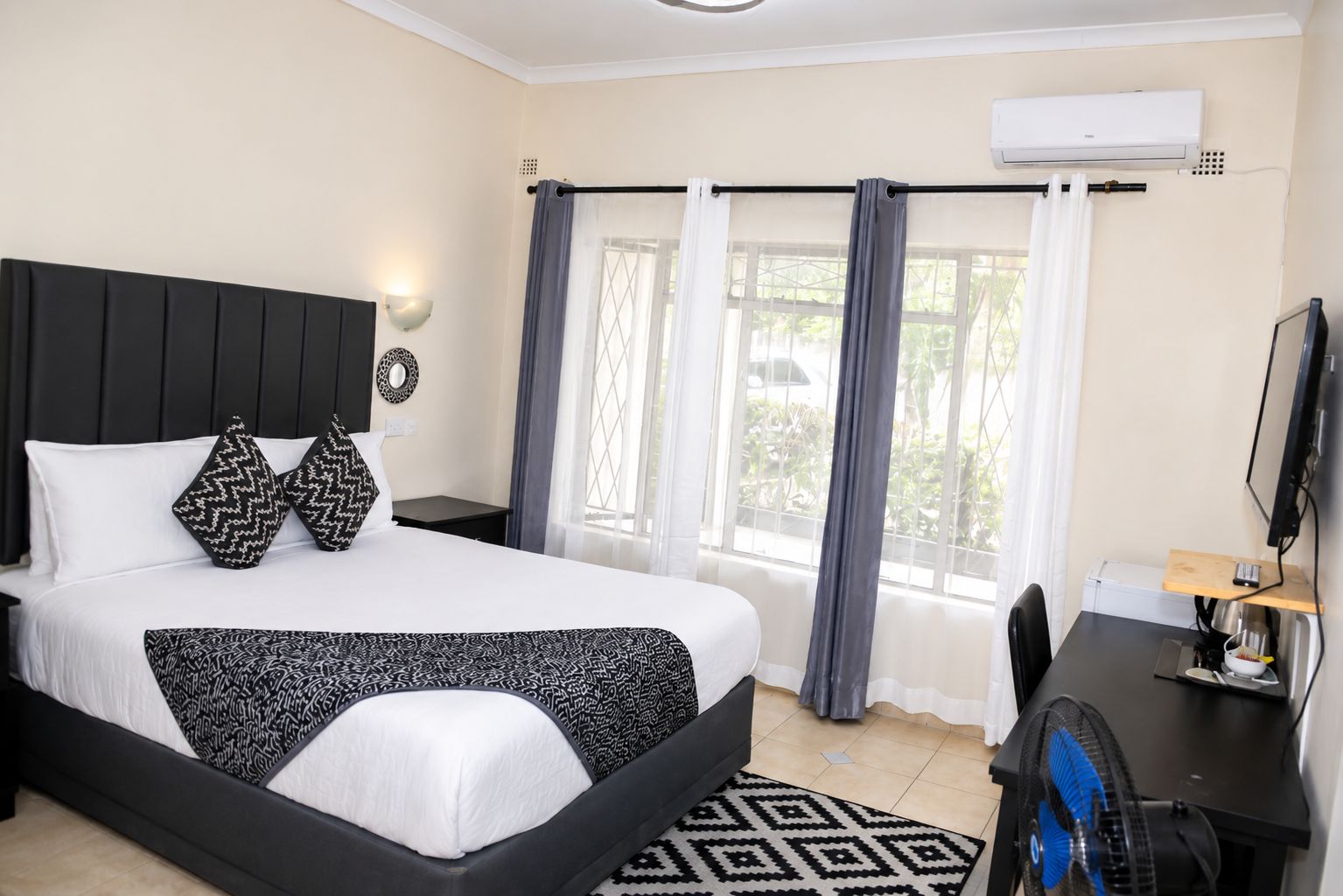 A hotel room with a bed, a desk, a chair, a TV, and a window with curtains.