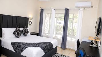 A hotel room with a bed, a desk, a chair, a TV, and a window with curtains.