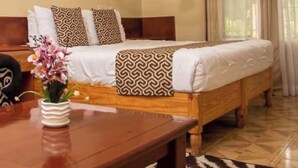 A neatly arranged bedroom with a wooden bed, patterned pillows, a bedside table with a vase of flowers, and a hanging light fixture. - Wild Trekkers Lodge (Victoria Falls)