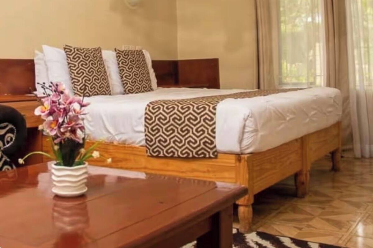 A neatly arranged bedroom with a wooden bed, patterned pillows, a bedside table with a vase of flowers, and a hanging light fixture.