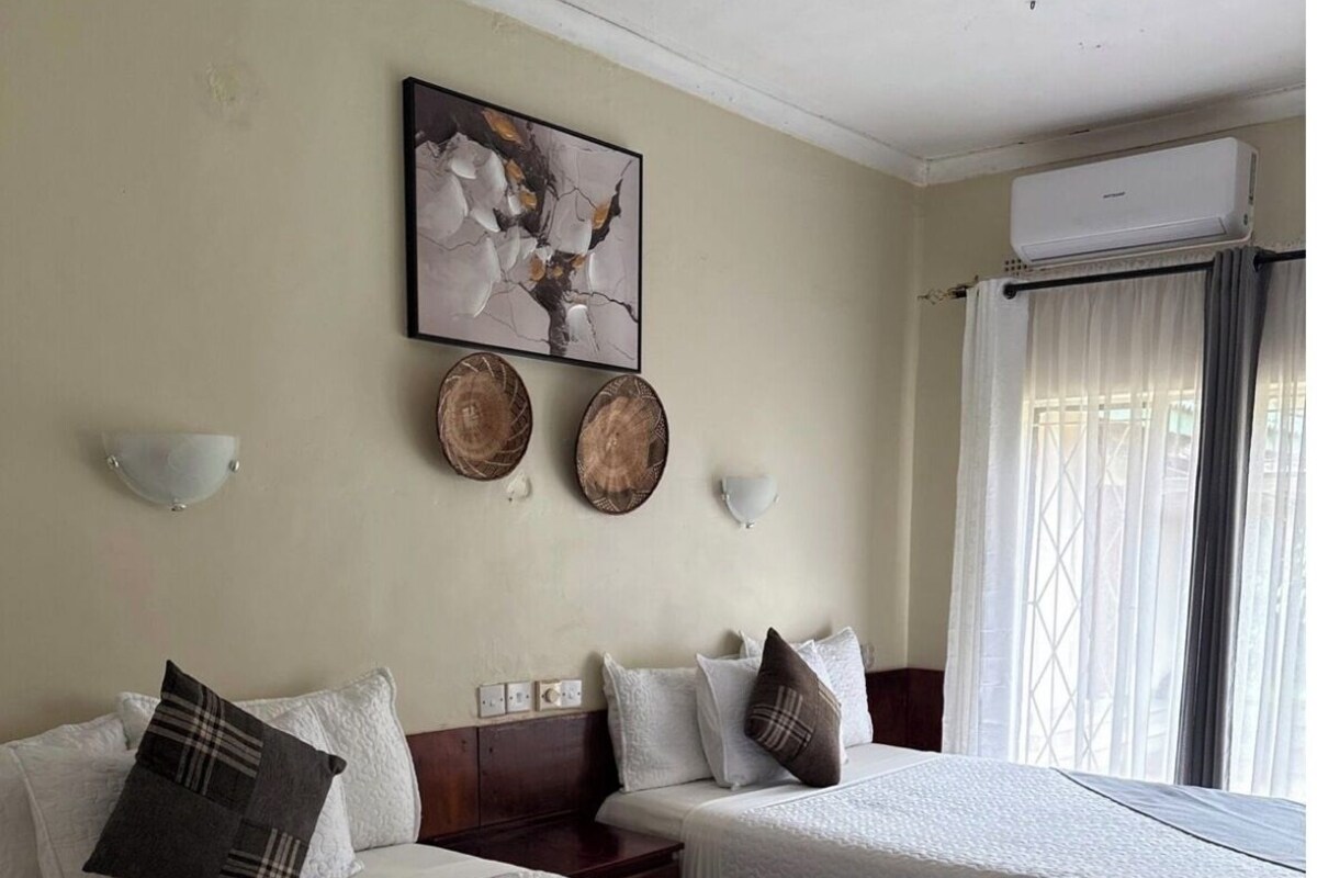 A hotel room with two beds, a painting, wall sconces, and a window with curtains.
