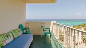 Een balkon met uitzicht op de oceaan, een blauwe bank en twee groene stoelen.