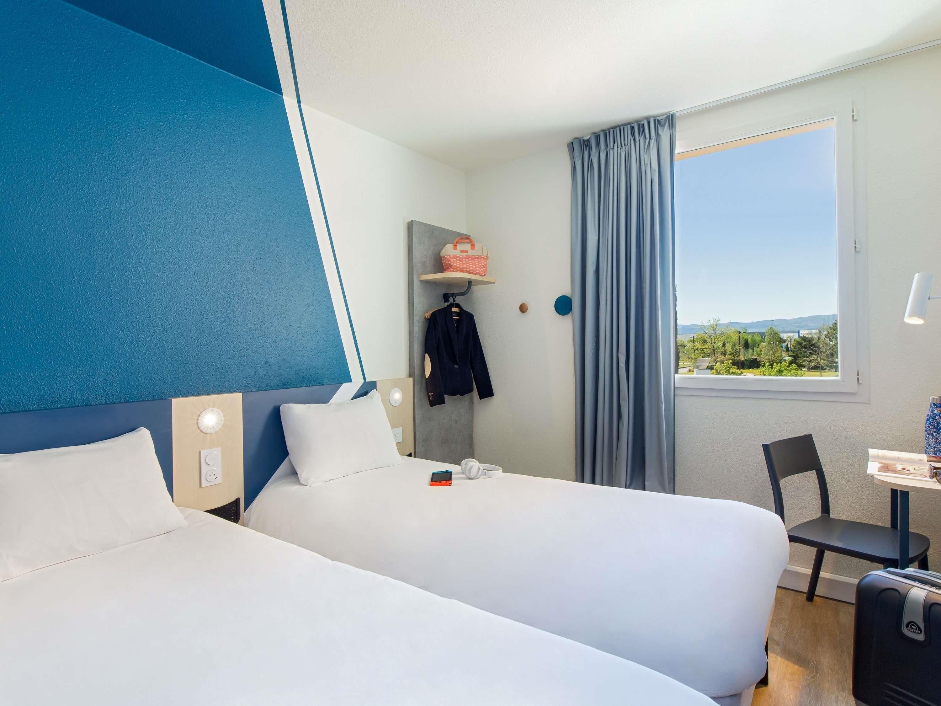 Habitación de hotel con dos camas, un escritorio, una silla y una ventana con vistas.