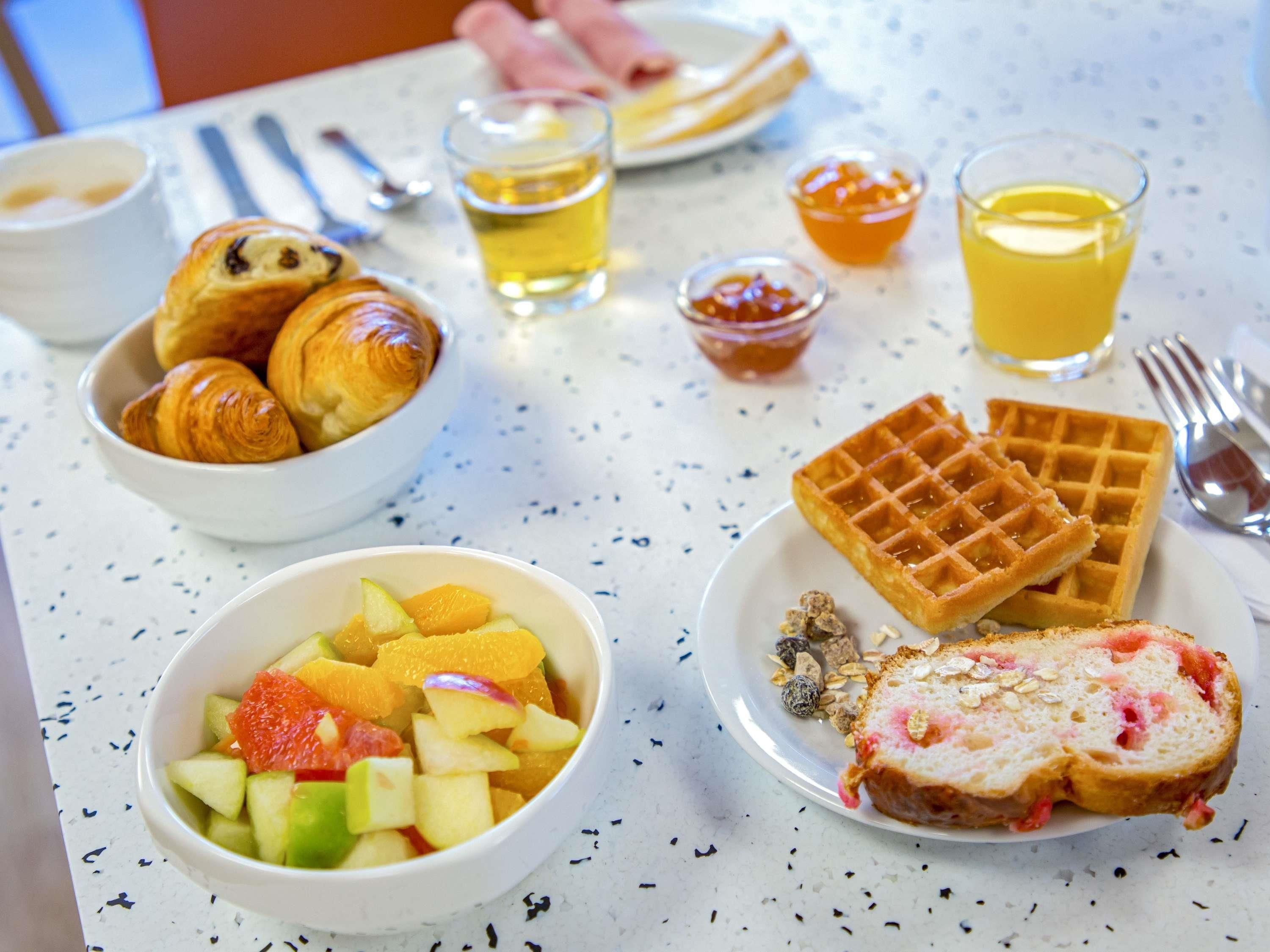 A breakfast table with croissants, waffles, fruit salad, and a slice of bread with jam.