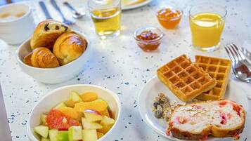 A breakfast table with croissants, waffles, fruit salad, and a slice of bread with jam.