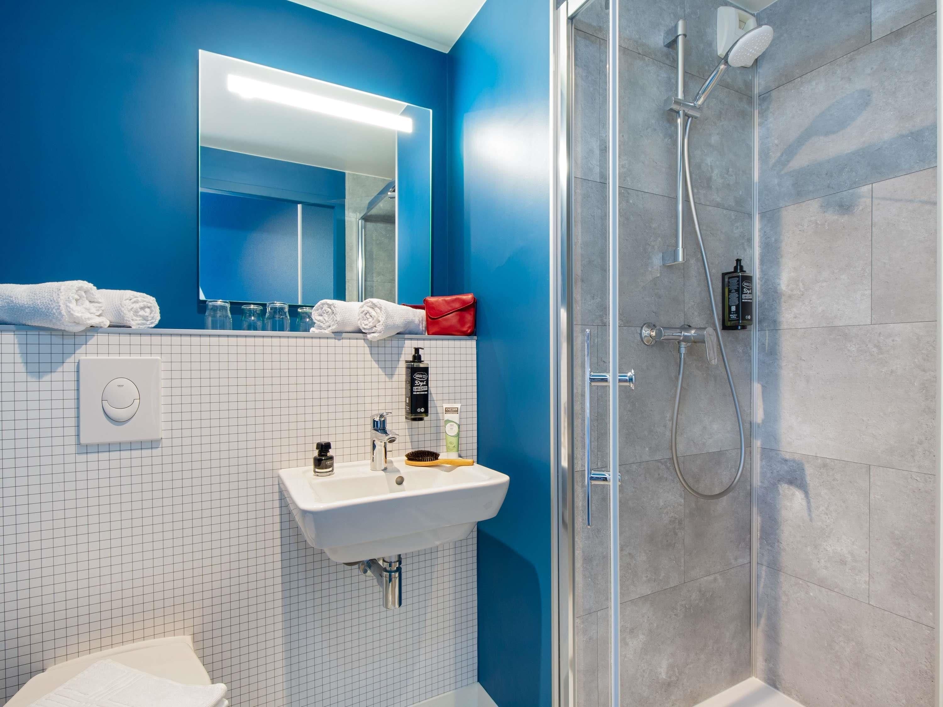 A modern bathroom with a glass shower enclosure, a white sink, and a mirror above it.