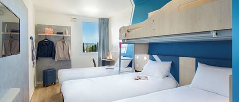 A hotel room with bunk beds, a suitcase, a mirror, and a window with a view.
