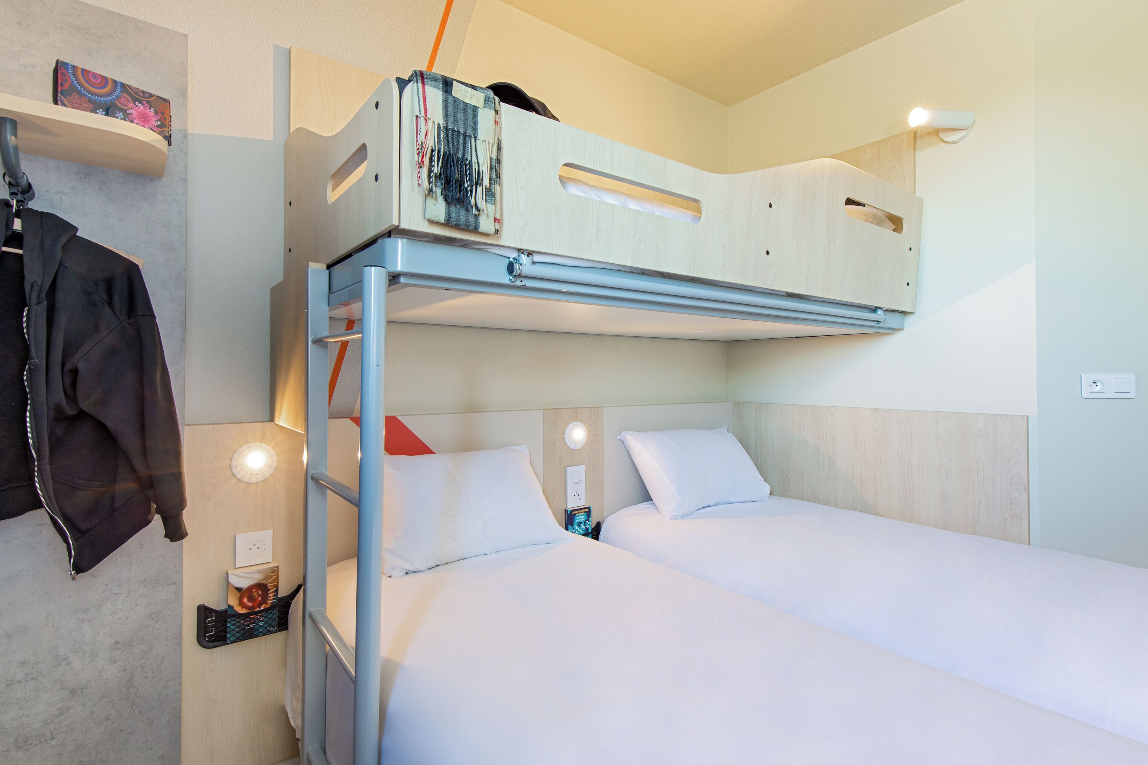 A bunk bed with a desk and a jacket hanging on the wall.
