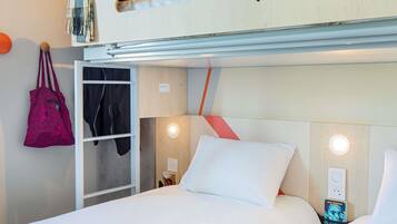 A hotel room with a bunk bed, a wardrobe, a bedside table with a lamp, and a wall-mounted power outlet.