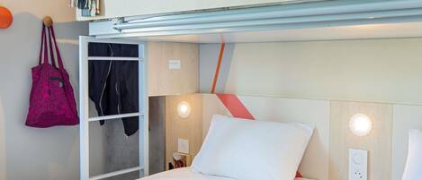 Una habitación de hotel con literas, un armario, una mesita de noche con lámpara y un enchufe en la pared.